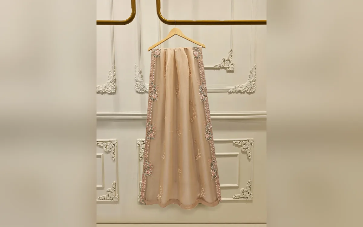 Sheer peach dupatta with floral embroidered borders hanging on a gold rail